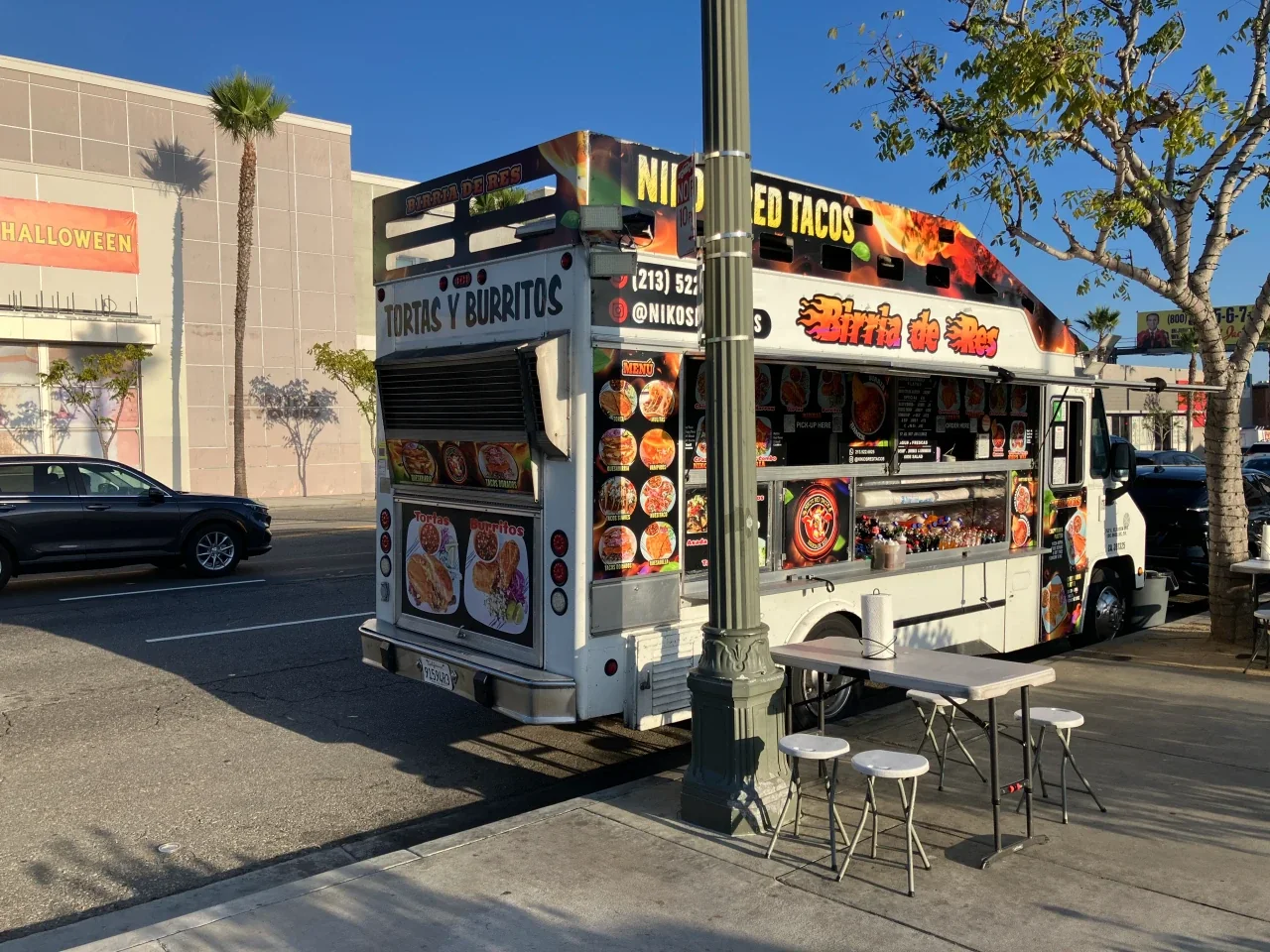 The Nikos Red Tacos truck parked curbside with a sidewalk table